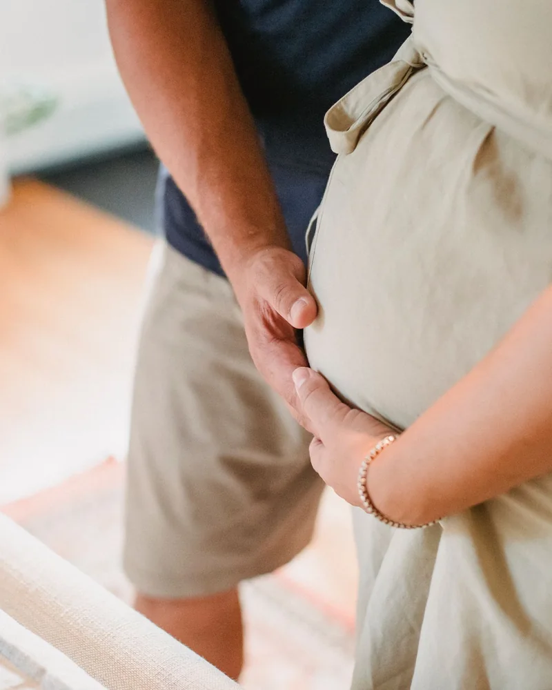 Two hands resting on a pregnant belly, the pregnant person's and their partner's