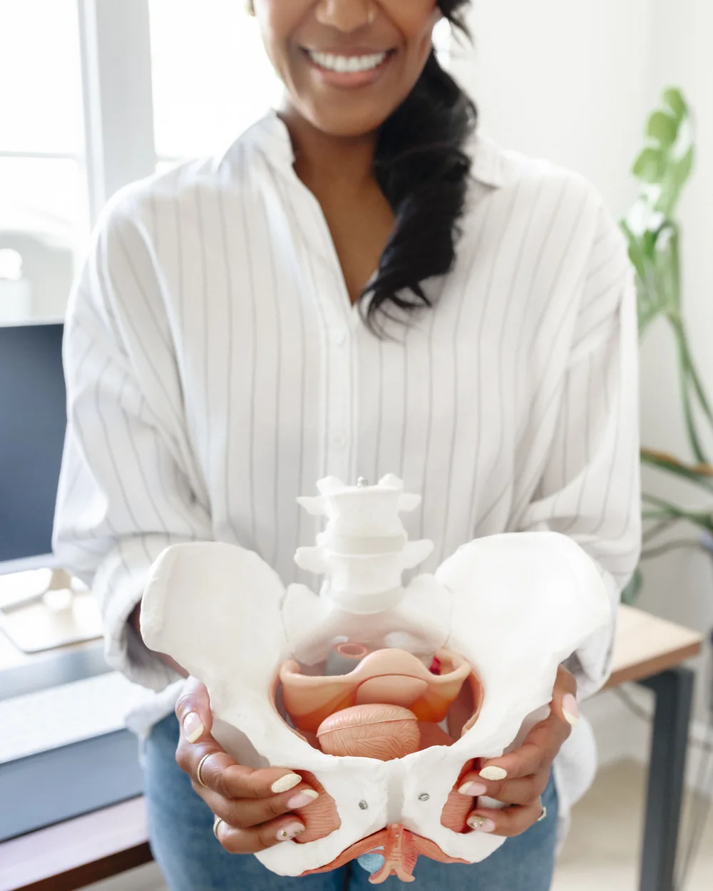 Karina Jackson, smiling, holds an anatomical pelvis model in front of her, the uterus visible inside