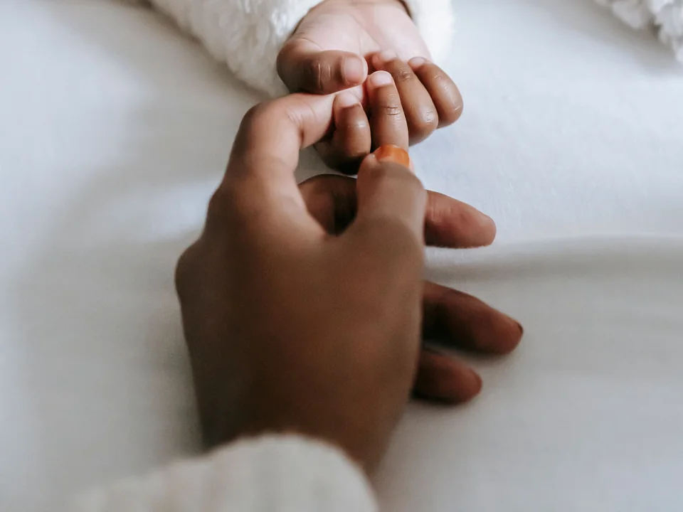La main d'une mère qui tient doucement la main de son bébé endormi, sur un lit blanc