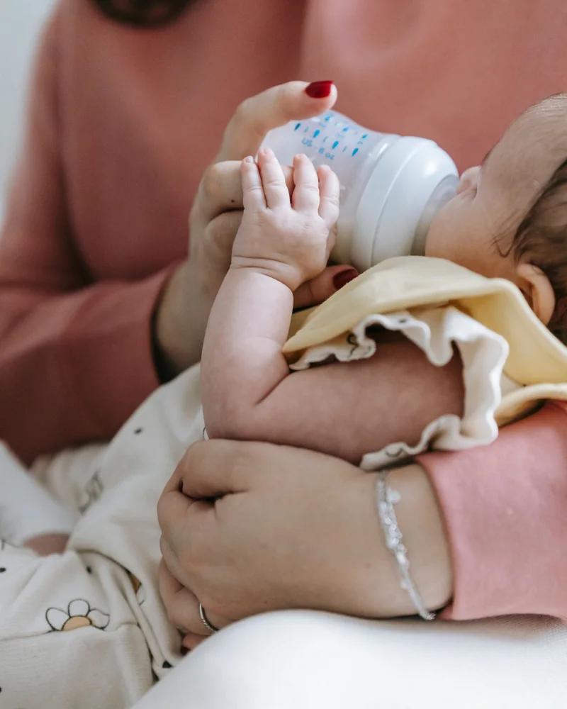 Un parent en chandail rose qui nourrit son nouveau-né au biberon, ses mains autour du bébé
